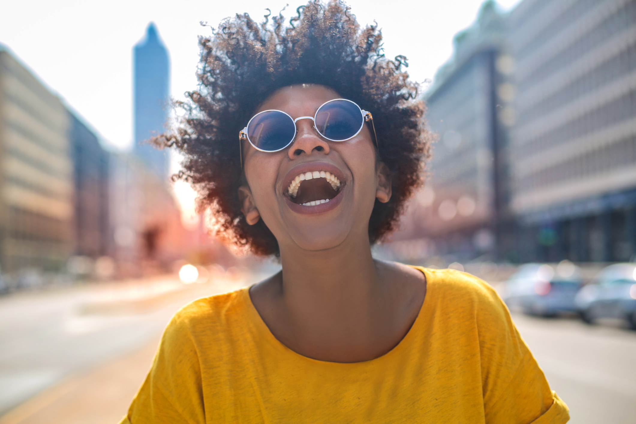 Healthy young woman with afro hair and round sunglasses enjoying the sun and the life of the city