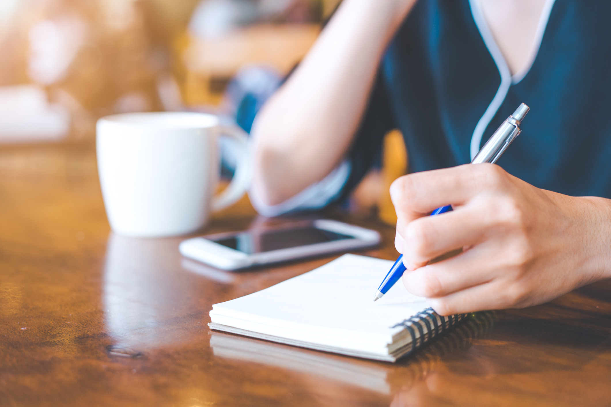 Business woman hand is on a notepad with a pen on a wooden desk in the office.