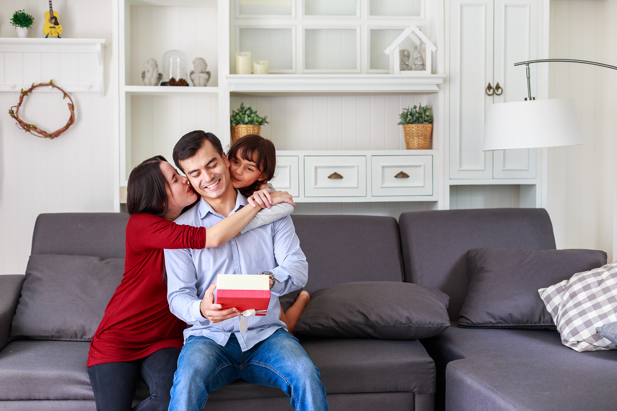 Daughter and mother surprising father with gift at home in the living room, Mother with kids celebrating father's day