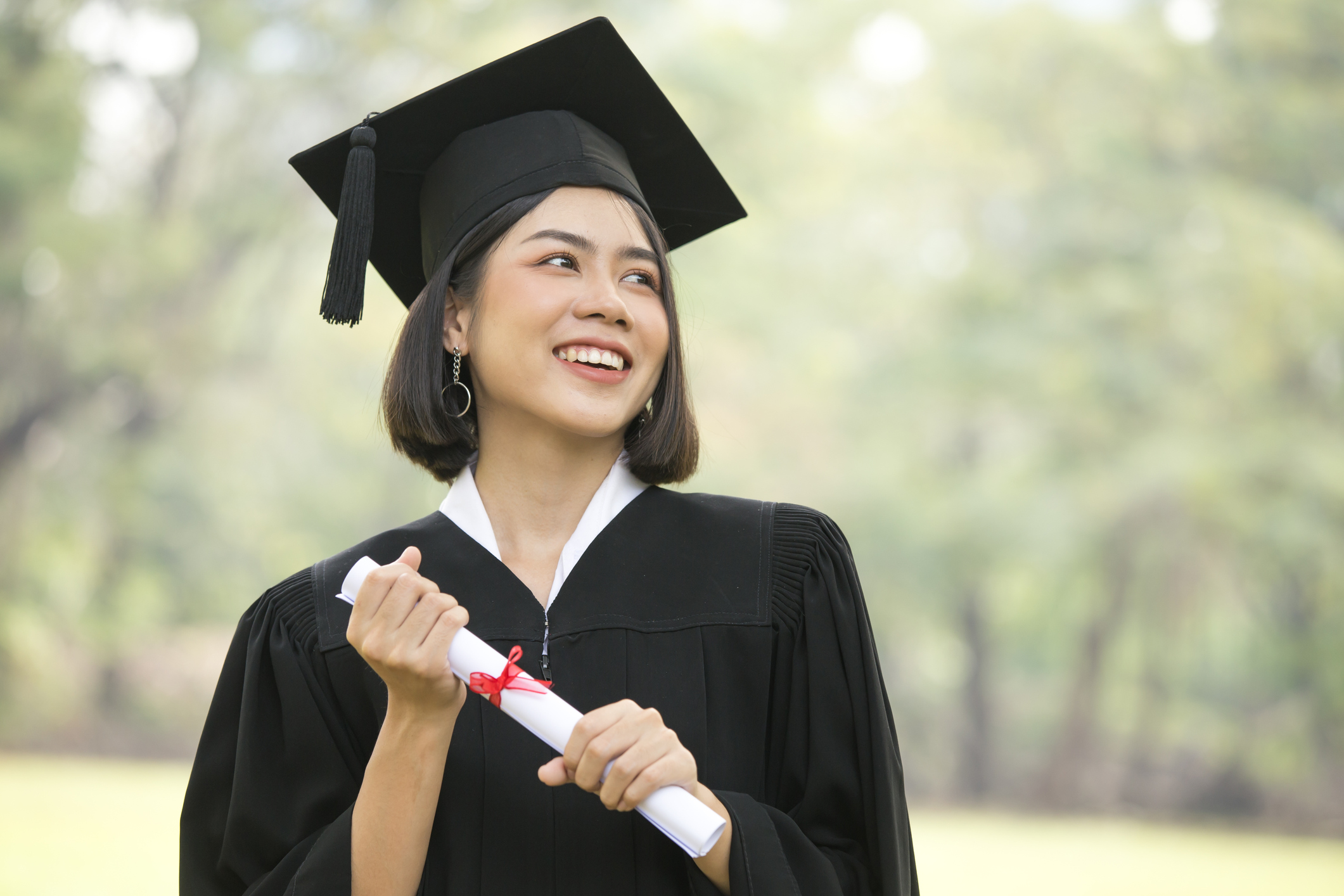 Young Asian Woman Students wearing Graduation hat and gown, Garden background, Woman with Graduation Concept.