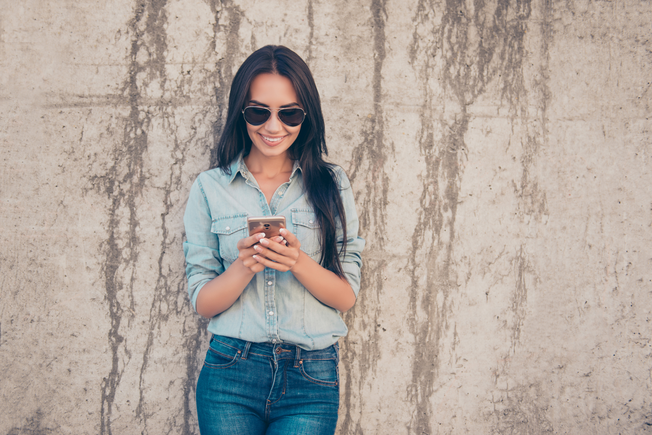 Attractive cheerful brunette woman reading sms near the stone wall and using 4g internet