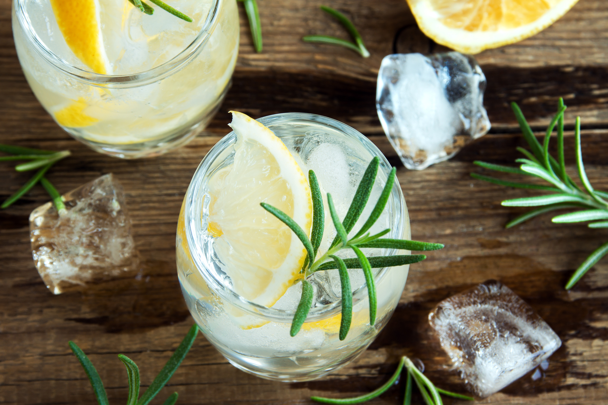 Alcoholic drink (gin tonic cocktail) with lemon, rosemary and ice on rustic wooden table, copy space