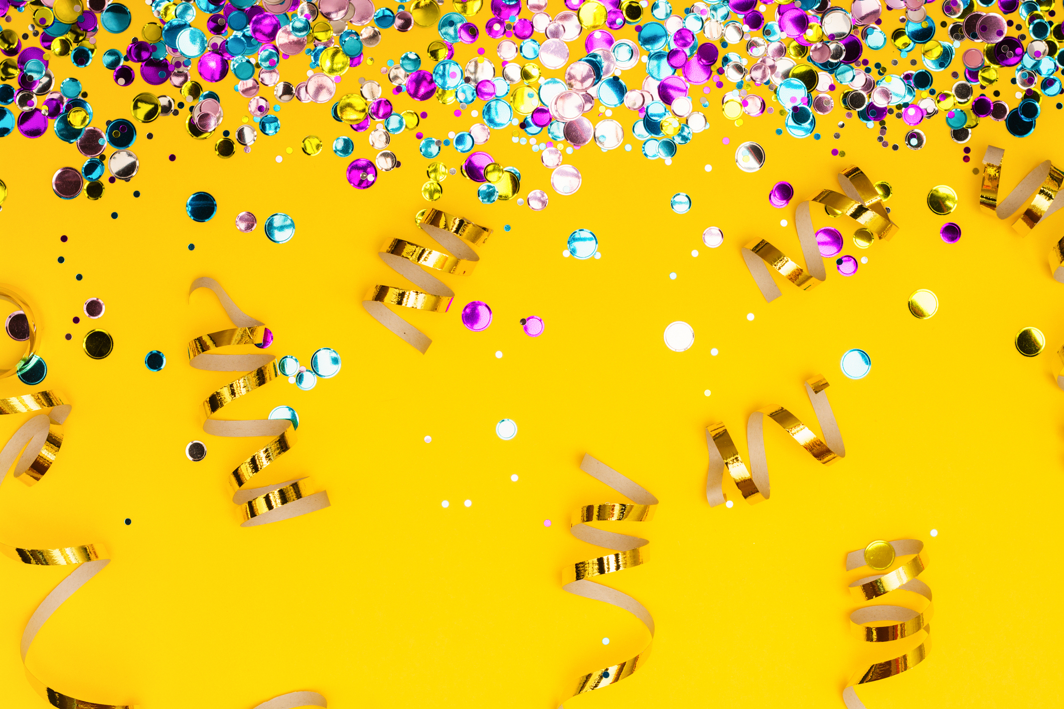 Colorful confetti and golden coiled streamers on yellow background. Festive party or carnival border. Copy space