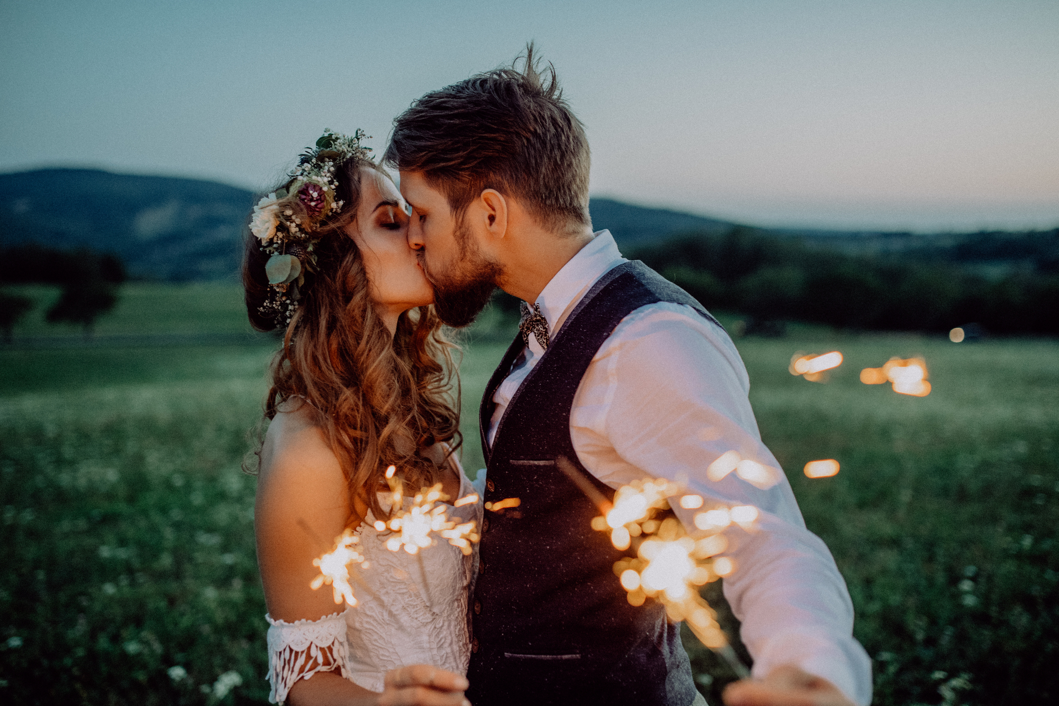 Beautiful young bride and groom on a meadow in the evening, holding sparklers.