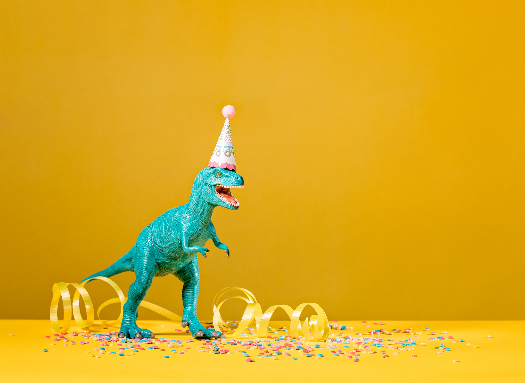 Toy dinosaur with birthday party hat on a yellow background.