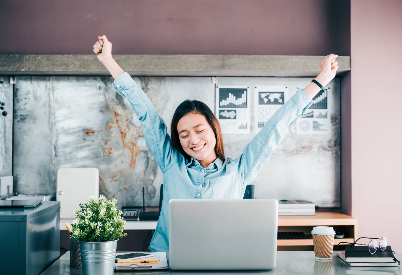 Asian creative designer raise arm up and close eye in front of laptop computer on desk,relax from hard work in office