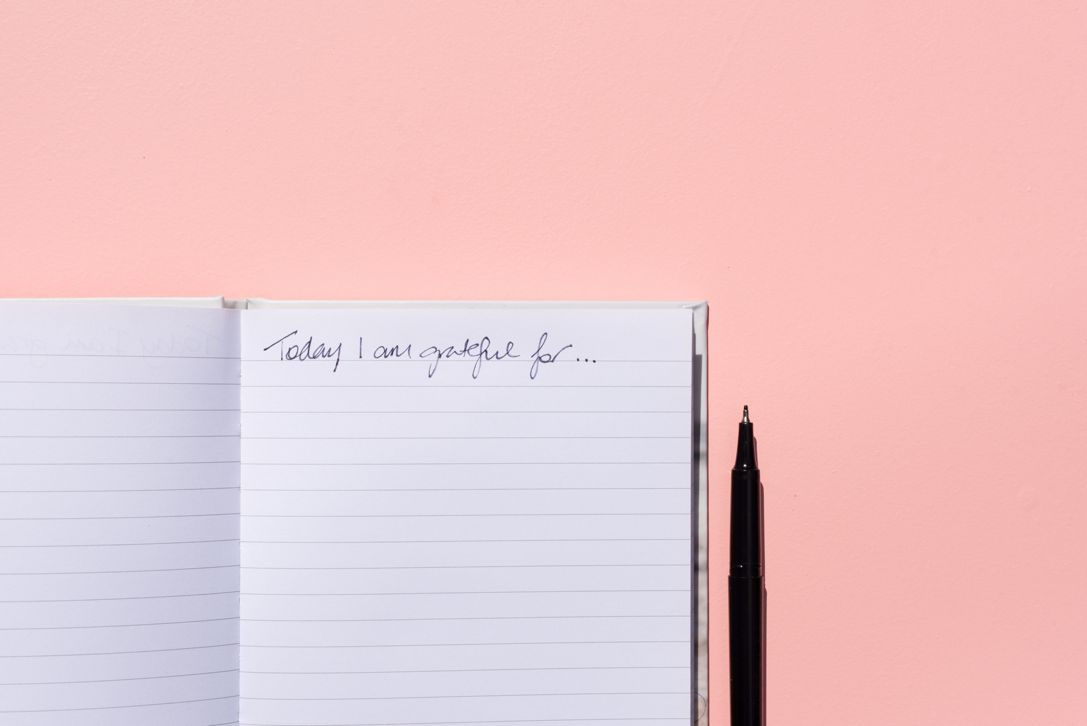 Gratitude journal and pen on pink background from above